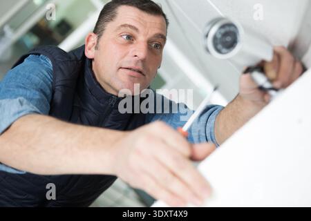 technician installing cctv camera on wall indoors Stock Photo