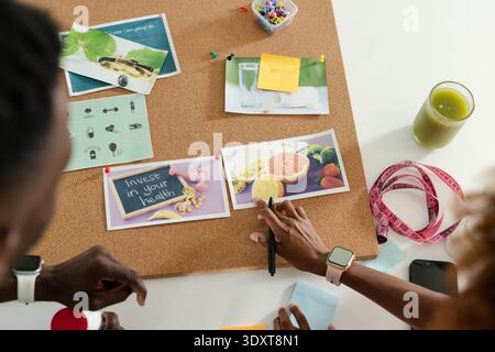Cork board is showcasing pinned fruit photos and health card on white table, with green juice Stock Photo