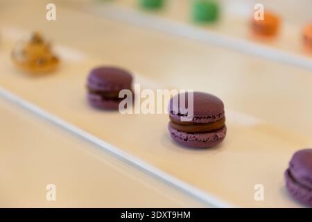 Purple macarons and assorted colorful pastries displayed on white tray. Stock Photo