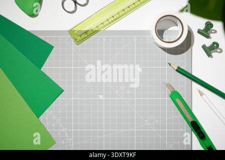 Creative craft workspace with green paper, utility knife, ruler, and tape on a grey cutting mat. Copyspace. Stock Photo