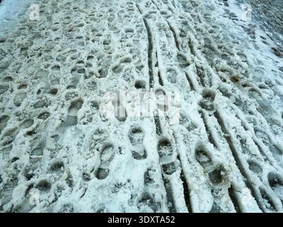 Numerous Footprints and Sled Tracks in Icy Slushy Snow. Textured Winter Surface with Dynamic Pattern. Copyspace. Stock Photo