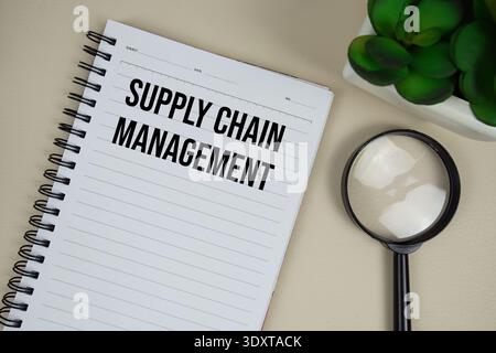 Supply Chain Management (SCM) text on paper notebook with magnifying glass on beige leather background Stock Photo