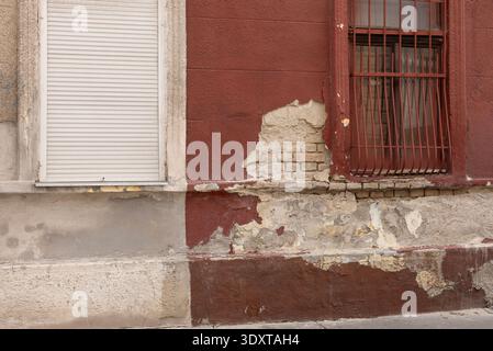 Distressed red facade with peeling plaster and iron security bars on window. Stock Photo