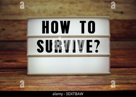 Lightbox with text "How To Survive?" on wooden background Stock Photo