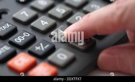 A person pressing buttons on a black office calculator for financial accounting or budget planning. Close up. Stock Photo