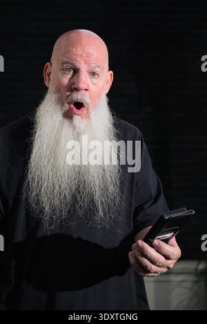 Portrait of old bald man with a long white beard using phone against a dark background Stock Photo