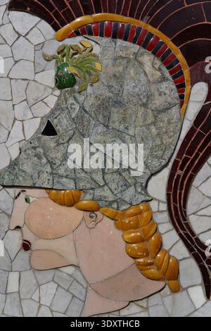 Intricate mosaic of a classical warrior profile with ornate helmet, braided orange hair, and green crest on the stone pavement in Nice's old town. Stock Photo