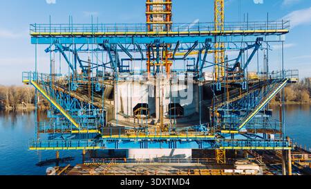 Aerial view of a bridge under construction reflecting in the water, its blue scaffolding contrasting the river's dark surface, Novi Sad, Vojvodina, Se Stock Photo