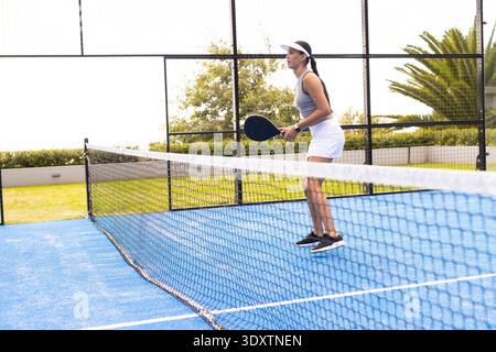 African American woman in white visor playing on court at net holding black paddle, copy space Stock Photo