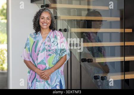 African American woman posing by floating stairs with glass panels in entry, wearing pastel kaftan Stock Photo