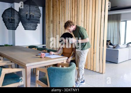 Couple leaning over paperwork at open-plan dining table with mugs and green chairs, copy space Stock Photo