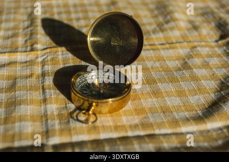 Golden compass on checkered fabric: navigational tool in sunlight. Stock Photo