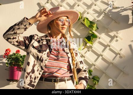 Fashionable woman in sun hat and sunglasses posing outdoors with floral background. Stock Photo