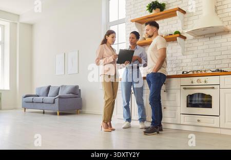 Young happy couple discussing contract with female realtor agent looking through the documents Stock Photo