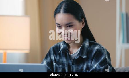 Smiling happy Asian Korean woman student freelancer typing on laptop at home working online browsing web Japanese female professional girl using Stock Photo