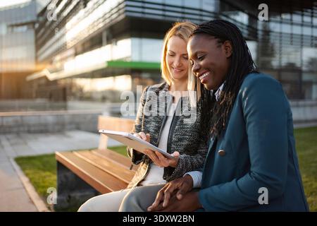 Two diverse businesswomen discussing data on digital tablet outdoors Stock Photo