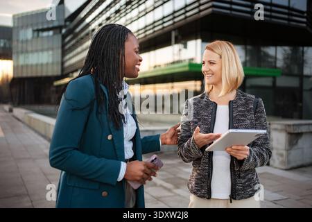 Diverse businesswomen discussing work using digital tablet outdoors Stock Photo