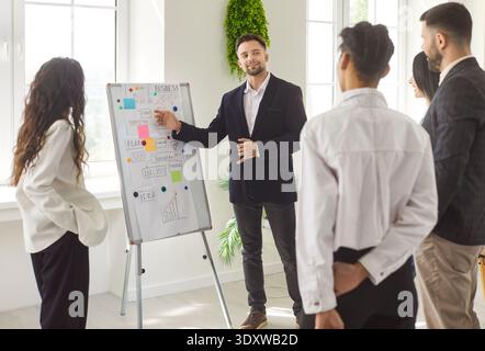 Man manager demonstrating something on whiteboard, colleagues listening to business presentation Stock Photo