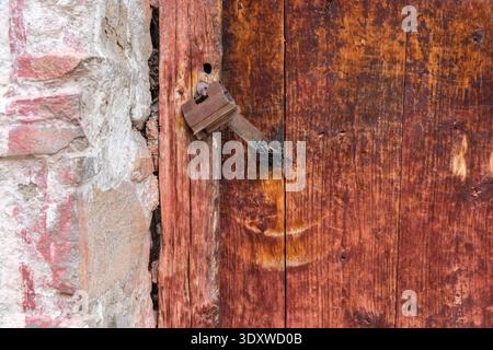 A close-up reveals a rusted metal latch and padlock securing an aged, reddish-brown wooden door at the historic Hemis Gompa. Stock Photo