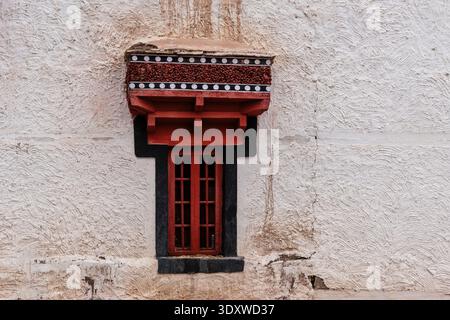A single traditional window with a decorative red lintel and white-dotted black trim sits centered on a lime-washed wall at Hemis Gompa. Stock Photo