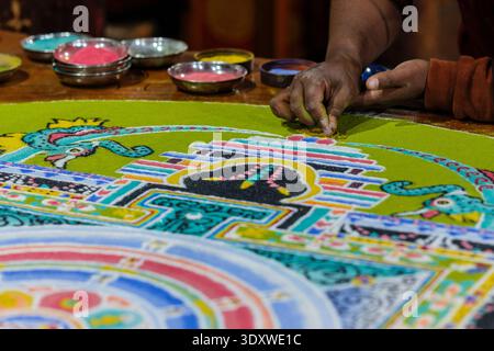 A hand carefully adds coloured sand to a complex pattern featuring a mythical creature on a mandala's edge at the Hemis Gompa. Stock Photo