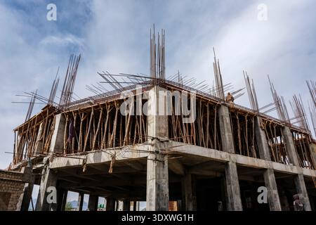 Construction site in Leh showing the concrete frame of a multi-storey building with wooden shoring and steel reinforcement bars. Stock Photo