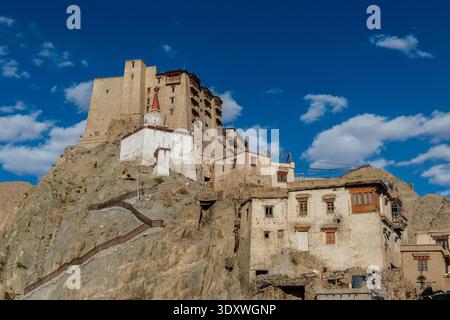 The historic Leh Palace and a white-washed Buddhist stupa stand prominently on a rocky outcrop under a deep blue sky with scattered clouds. Stock Photo