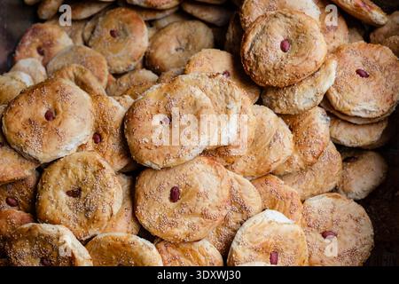 A pile of golden-brown baked traditional Girda breads, covered in sesame seeds and topped with a single almond, at a bakery in Leh. Stock Photo