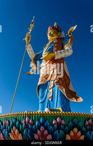 A detailed low-angle view shows the golden face and vibrant robes of the Guru Padmasambhava statue in Shey against a deep blue sky. Stock Photo