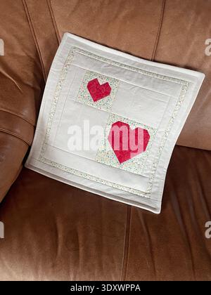 Handmade patchwork cushion cover in white cotton, featuring two red heart appliqués made with foundation paper piecing (FPP),delicate machine quilting. Stock Photo
