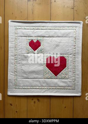 Handmade patchwork cushion cover in white cotton, featuring two red heart appliqués made with foundation paper piecing (FPP),delicate machine quilting. Stock Photo