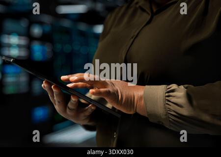 Close up of admin holding tablet walking through server room rows lined with storage hardware. IT expert using device app to inspect data center helping power internet services for business clients Stock Photo
