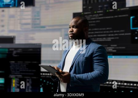 African American developer working on programming and automation, coding on a laptop with a futuristic interface behind him. Tech professional thrives in a world of AI and code snippets. Stock Photo