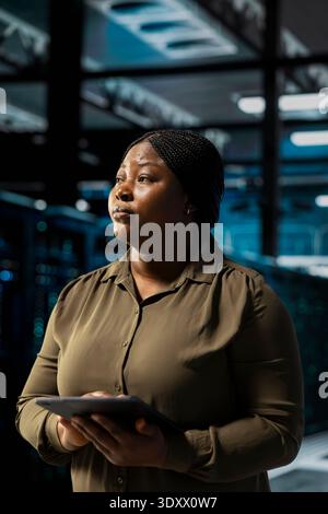 Data center software developer installing and configuring hardware used for hosting digital services. African american server room worker testing and repairing rigs managing file transfers Stock Photo
