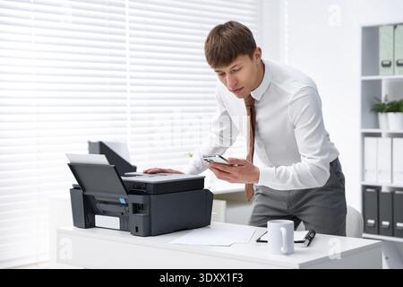 Man using printer and smartphone at white desk in office Stock Photo