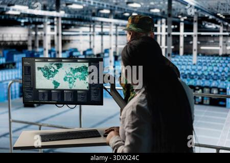 Military expert in data center briefing command officer using live world map analytics. Army units in server farm updating mission parameters based on world map intelligence feed Stock Photo