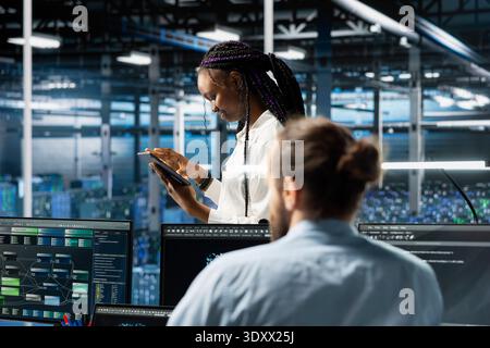 Data center system administrator working on databases supporting AI applications. African american woman in server hub conducting experiments on artificial intelligence algorithms improvements Stock Photo