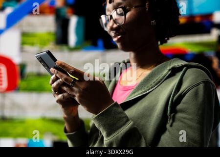 Close up of woman browsing social media feed on smartphone in front of digital video wall. Person using mobile phone, floating icons highlight interactive engagement online Stock Photo
