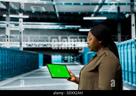 Data center technician conducts tests on hardware using isolated screen tablet to fix bugs. Server hub expert uses mockup device to refine algorithms for faster processing, updating core services Stock Photo