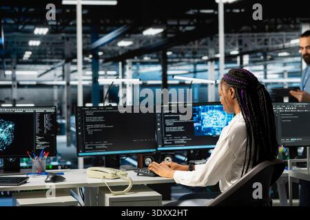 Software developer working in server farm with hardware supporting data mining. African american woman in data center using PC to do maintenance on racks storing blockchain records Stock Photo