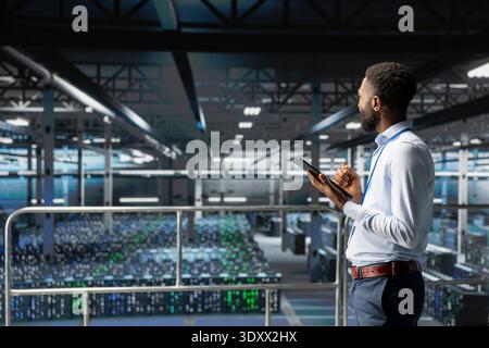 African american engineer reviews performance outputs and AI visualizations on computer. IT expert analyzing neural network to ensure stable infrastructure operations in data center. Stock Photo