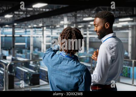 Black data center engineering team on industrial platform collaborating for server management, server rigs innovation. Technicians coordinating infrastructure tasks to support machine learning. Stock Photo
