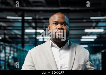Admin in high tech data center doing maintenance to prolong gear life span and avoid downtime. African american server hub IT professional monitoring infrastructure supercomputers Stock Photo