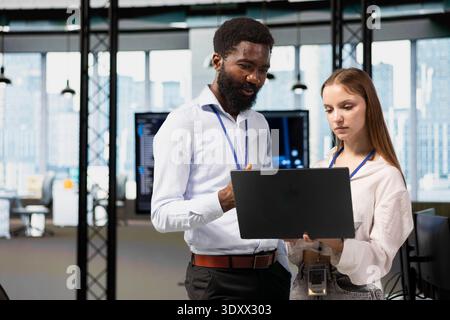 Manager helping young trainee coding during internship in tech startup using laptop. Team leader providing support to newcomer engineer using notebook in software development agency Stock Photo