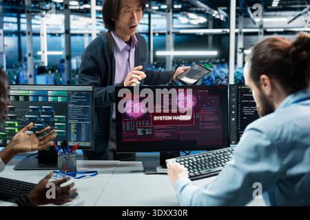 Manager supervising server farm admins alerted by hack warning, securing systems from cyberattack accessing confidential data. Teamworking data center colleagues defending rigs during security breach Stock Photo