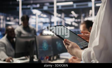 Close up of data center system administrator coding on tablet, doing software updates. Server room IT expert looking at device screen, optimizing infrastructure rackmounts configuration rigs, camera A Stock Photo