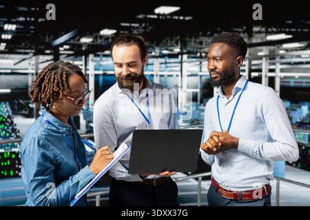 Multiethnic employees team collaborating on maintenance for server rigs and handling AI processing tasks. Data center engineering team supporting machine learning for software development. Stock Photo