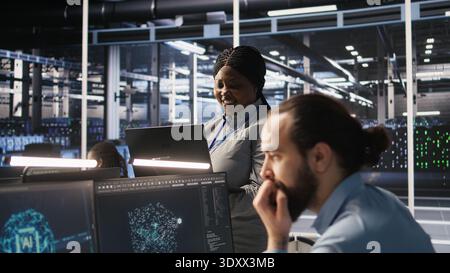 Data center system administrator pleased by neural network outputs after completing software updates. IT expert smiling, looking at laptop screen, optimizing configuration server hub rigs, camera A Stock Photo