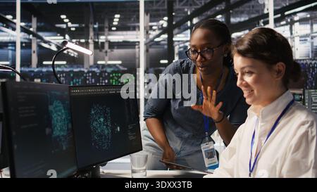 Cheerful data center engineers doing fist bump after completing successful AI system deployment. Smiling coworkers celebrating after achieving optimal machine learning model performance, camera A Stock Photo