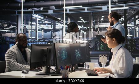 Server hub supervisor overseeing computer scientists improving neural network algorithms. Data center manager reviewing performance of employees doing checkup on infrastructure, camera A Stock Photo